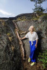 Liia Kaitanen nojaa kallion kolossa olevaan pystysuoraan puun juureen