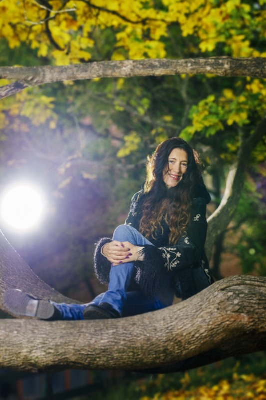 Angela Nicoletti istuu hymyillen vehreässä puistossa olevan puun paksulla oksalla