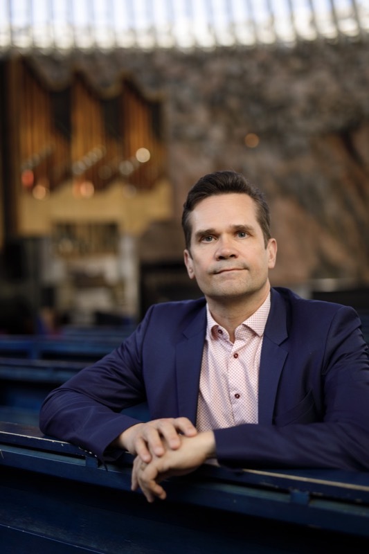 Mika Aaltola istuu Helsingin Kallion kirkon penkissä taustalla kirkon urut