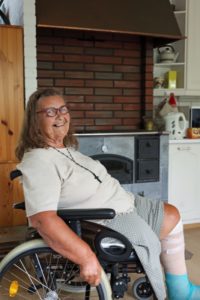 Hellin Laine istuu iloisena pyörätuolissa kotinsa keittiön puuhellan edustalla