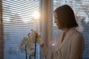 Päivi Voima pitää käsissään ja katselee orkideaa ikkunan edessä