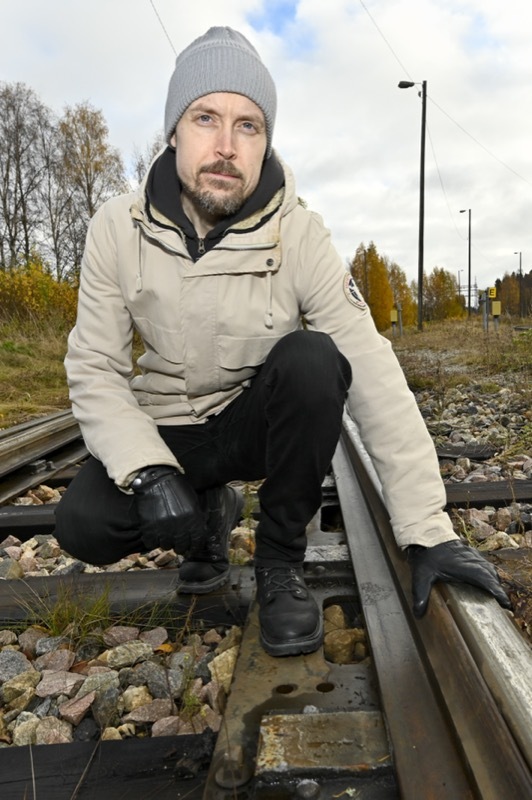Lauri Kemppainen kumartuneena Kajaanin kaupungin reunamilla olevan teollisuusraiteiden välissä