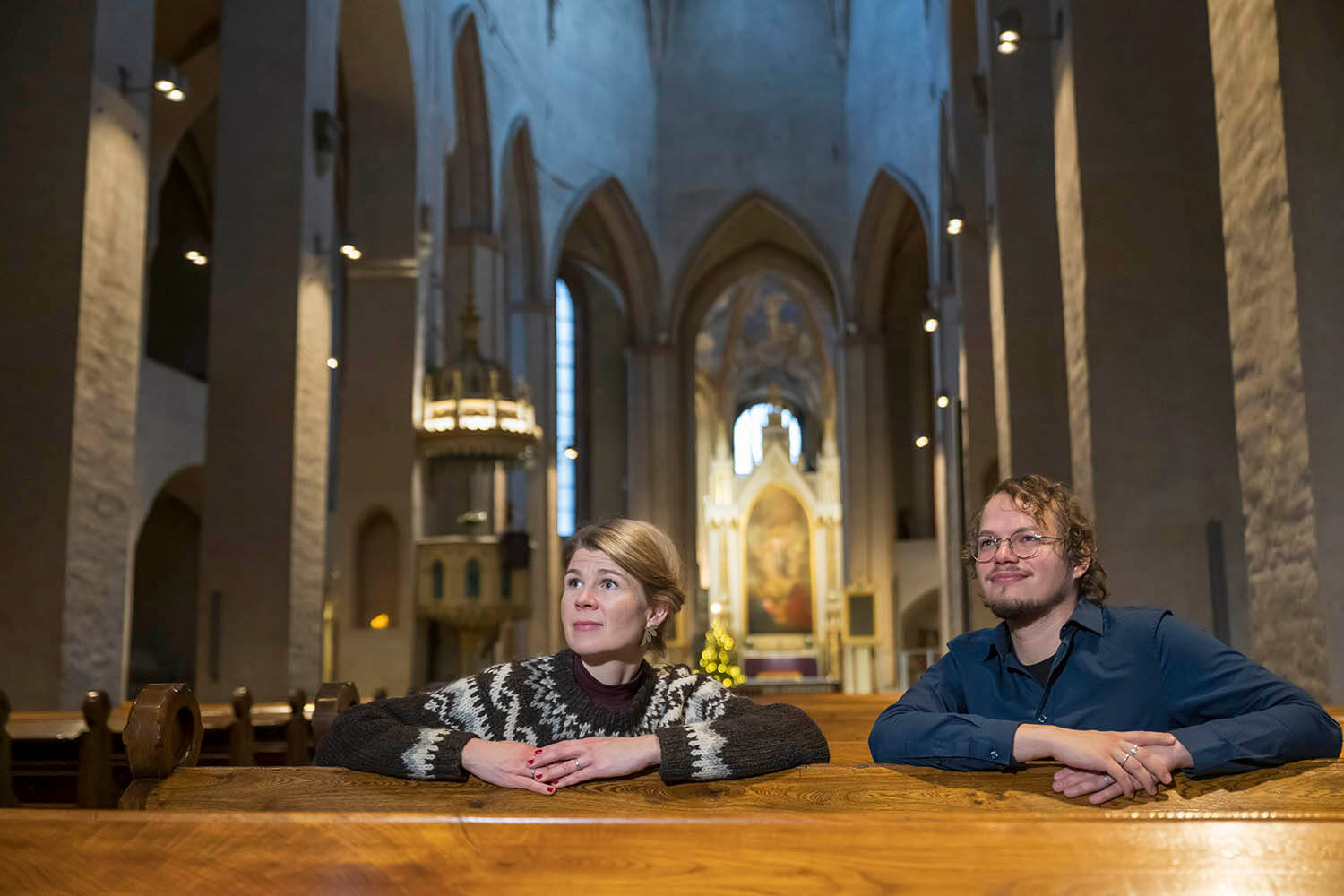 Annastiina Papinaho ja Ilari Aalto istuvat penkissä Turun tuomiokirkossa kääntyneinä katsomaan taaksepäin niin, että alttari näkyy taustalla. Sana-lehti