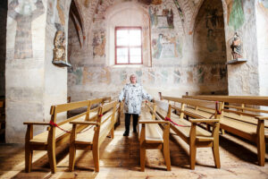 Anneli Kanto seisoo Hattulan Pyhän Ristin kirkossa penkkien välissä taustalla värikkäät seinämaalaukset 1500-luvulta.