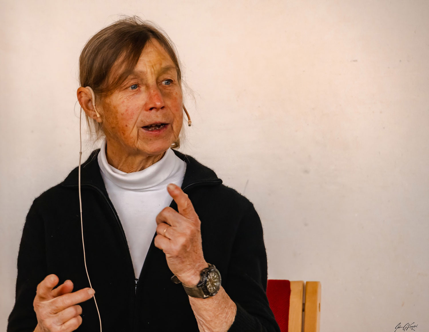 Cynthia Bourgeault istuu tuolissa, hänellä on korvanappikuulokkeet, ja hän puhuu jollekin, kädet ovat ilmeikkäässä asennossa.