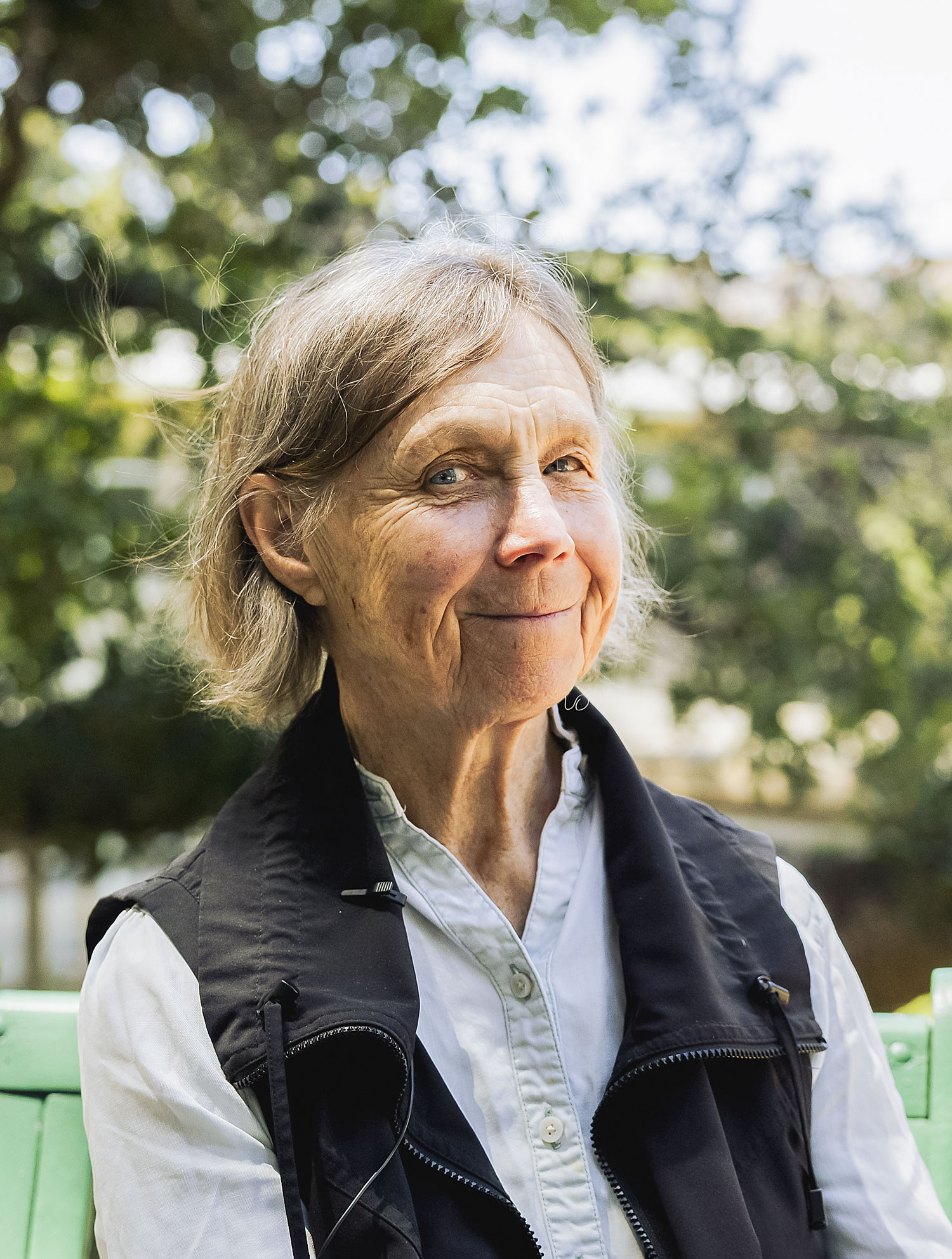 Cynthia Bourgeault poseeraa hymyillen kameralle, hän istuu ja kuvassa näkyy kasvot ja rintakehä, taustalla vehreitä puita.